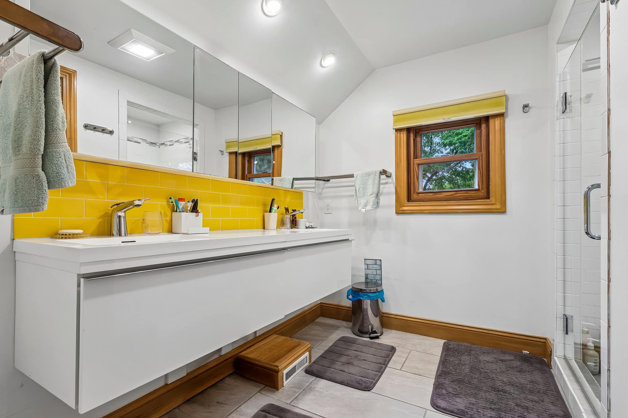 A modern bathroom features a white floating vanity with a bright yellow tiled backsplash and a shower stall.
